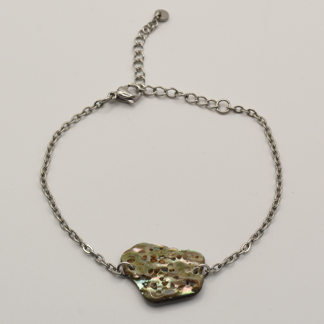 The Paua Shell Hihiri bracelet by Salty Dreamers features a delicate silver chain and an organically textured, flat metallic pendant with ocean-inspired holes, showcased on a plain white background.