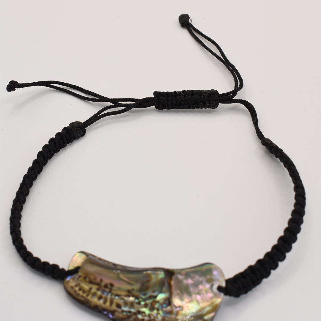 The Paua Shell Ngakau bracelet by Salty Dreamers is a handmade black adjustable braided cord accessory, featuring a shiny New Zealand abalone centerpiece, shown on a white background.