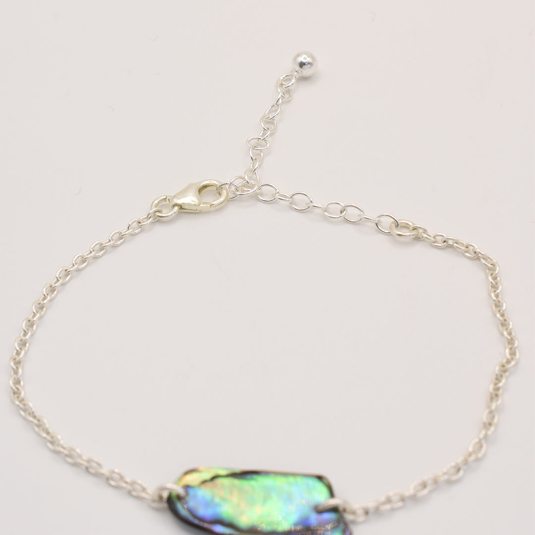 The Salty Dreamers Bracelet | Paua Shell Toi features a handmade silver chain and an iridescent New Zealand paua shell centerpiece, with an adjustable clasp, shown on a plain white background.