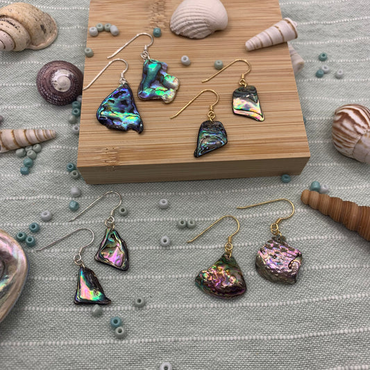 A display of Salty Dreamers' Earrings | Paua Shell Surprise—five pairs with gold hooks on green striped cloth, surrounded by seashells and beads—perfect for your favourite jewellery bag.