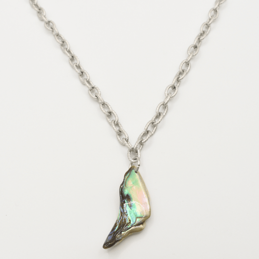 The Salty Dreamers Necklace | Paua Shell Hau is a silver stainless steel piece with a single iridescent pāua shell pendant, shaped like a small wing or shard, shown on a white background.