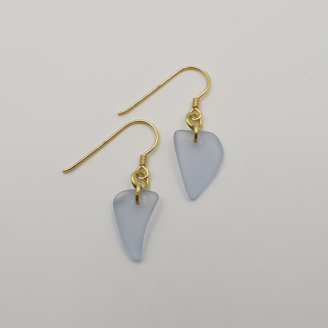Salty Dreamers' Earrings | Seaglass Small Blue feature handmade, irregular triangle pendants made from translucent light blue seaglass and gold hooks, shown on a plain white background.