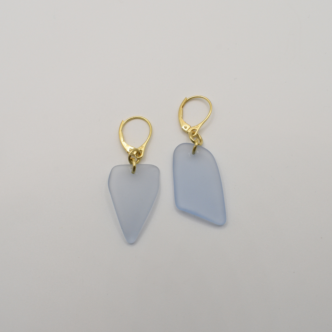 Salty Dreamers' "Earrings | Seaglass Blue-Sky" feature two gold-plated 925 silver earrings with irregular, frosted light blue pendants, displayed on a plain white background.