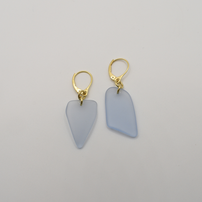 Salty Dreamers' "Earrings | Seaglass Blue-Sky" feature two gold-plated 925 silver earrings with irregular, frosted light blue pendants, displayed on a plain white background.