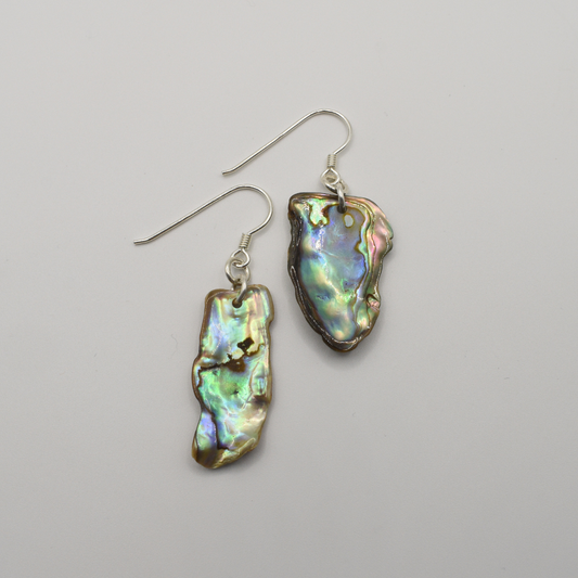 Salty Dreamers' Earrings | Paua Shell Kekeno feature handmade, irregular iridescent pāua shell pendants with silver hooks—an elegant showcase of New Zealand abalone jewelry, displayed on a plain white background.