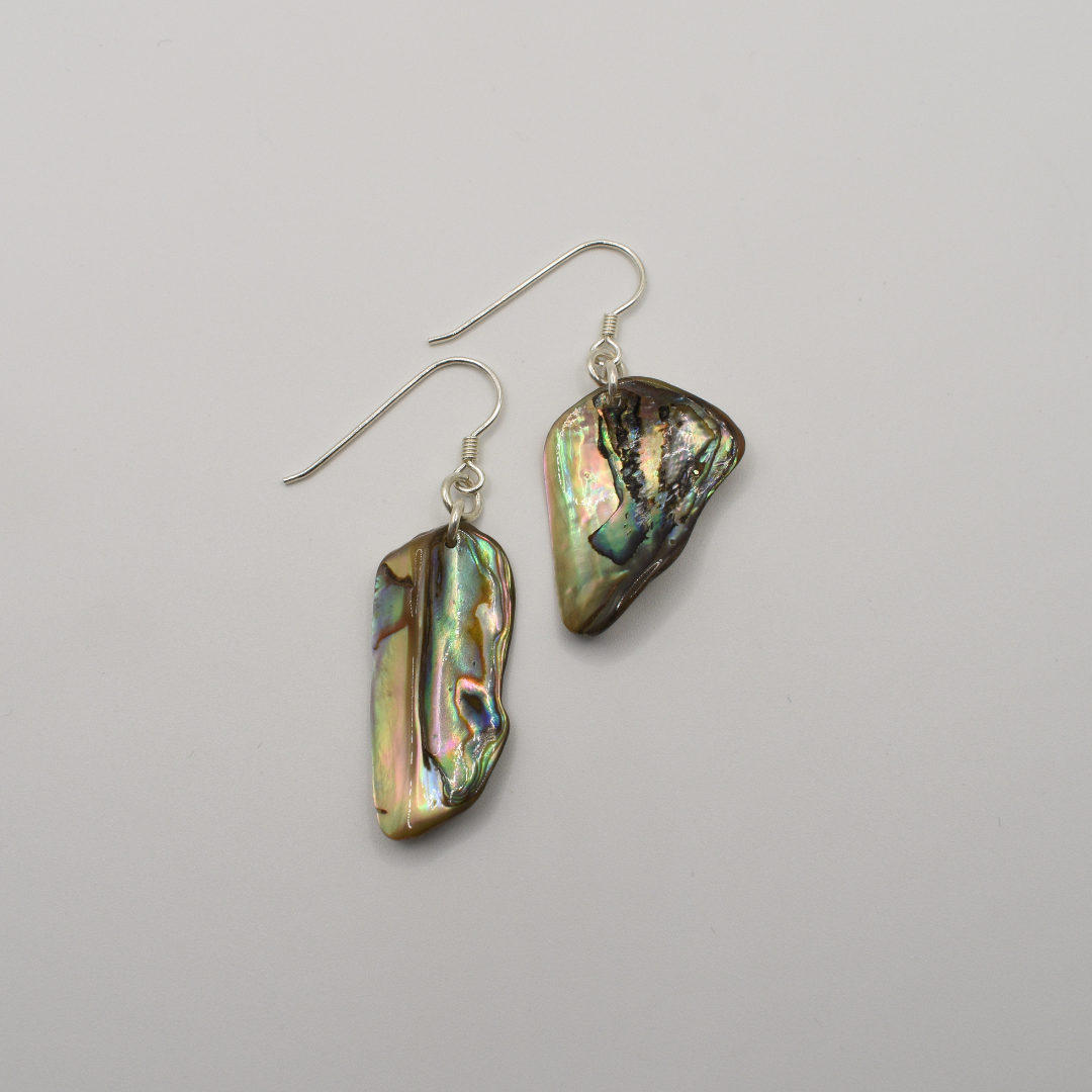 Salty Dreamers’ Earrings | Paua Shell Tieke: Handmade silver dangle earrings with iridescent, irregular pāua shell pieces on silver hooks, shown against a plain white background.