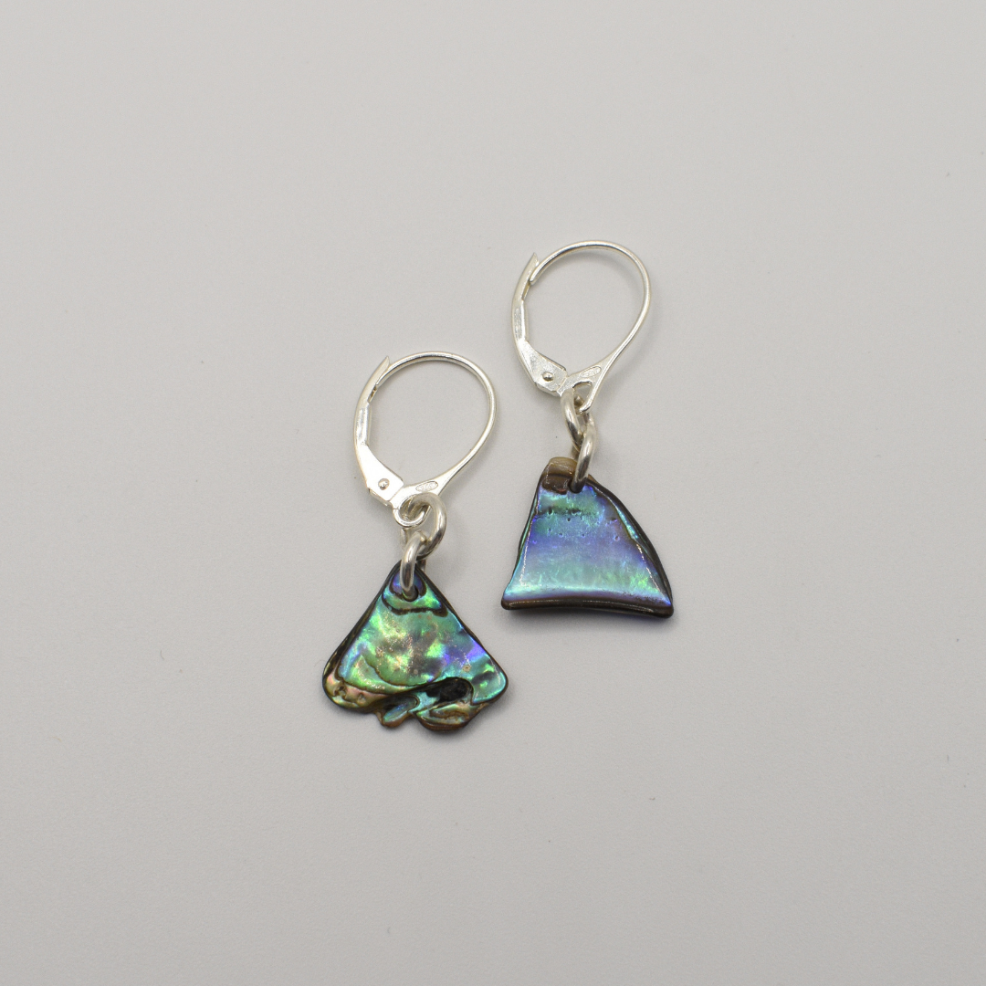 Salty Dreamers’ Earrings | Paua Shell Ngaru feature mismatched handmade earrings crafted from iridescent New Zealand abalone shell—one triangle, one irregular—set on silver lever-back hooks.