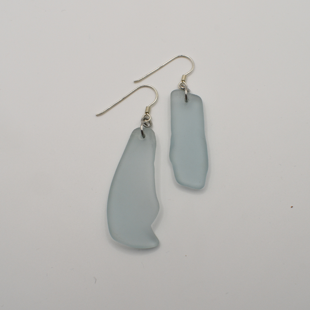 The Salty Dreamers Earrings | Seaglass Blue Surfer feature irregular frosted light blue glass pieces on simple metal hooks, shown against a plain white background.