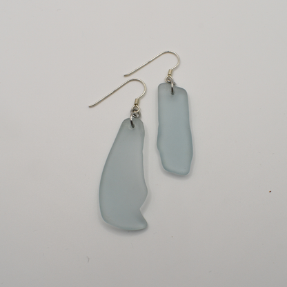 The Salty Dreamers Earrings | Seaglass Blue Surfer feature irregular frosted light blue glass pieces on simple metal hooks, shown against a plain white background.