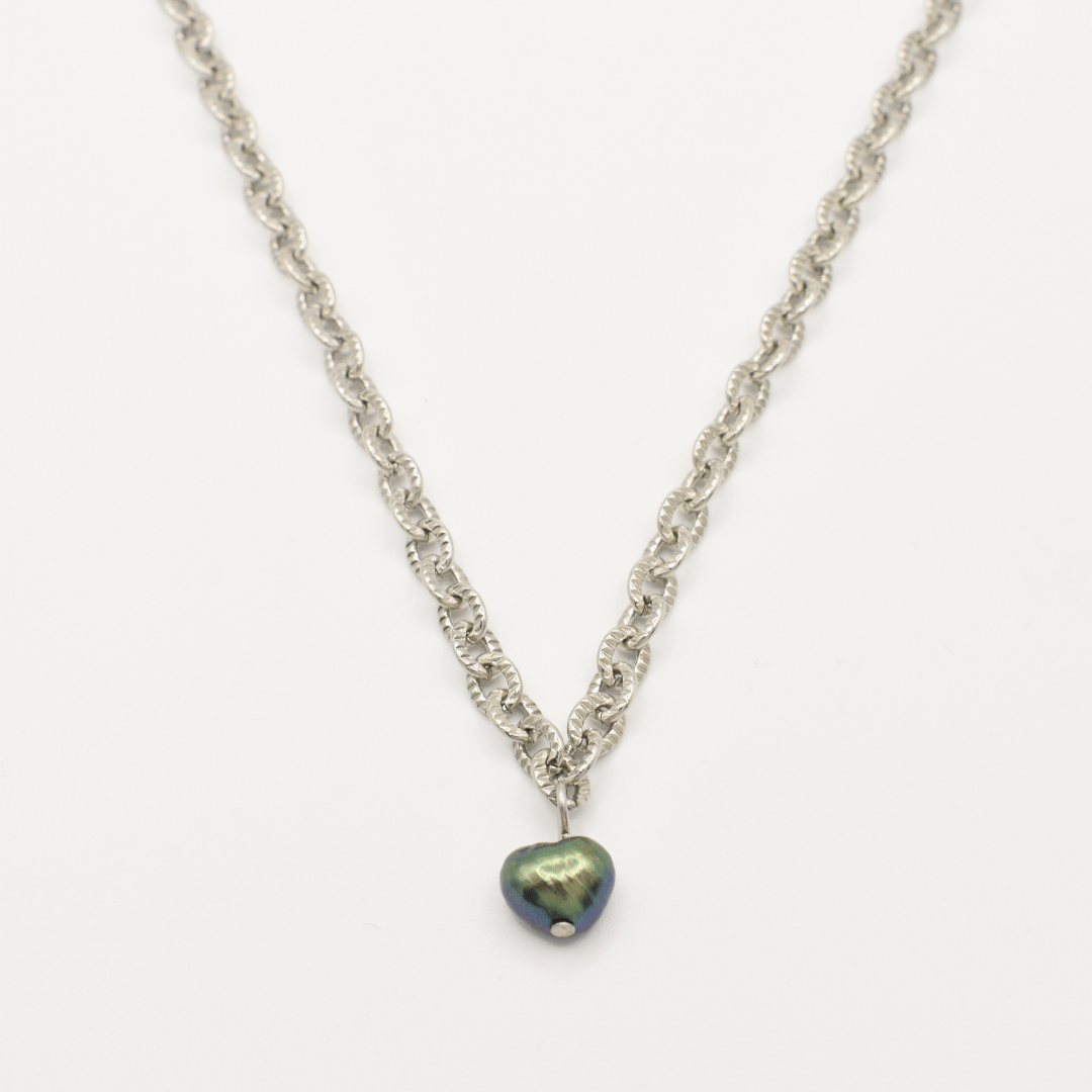 The Salty Dreamers "A Beach Pearl" necklace features a silver chain with a dark iridescent heart pendant and freshwater pearl accents, shown on a white background for surfer-inspired style.