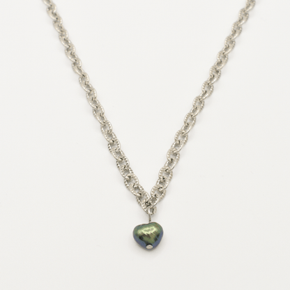 The Salty Dreamers "A Beach Pearl" necklace features a silver chain with a dark iridescent heart pendant and freshwater pearl accents, shown on a white background for surfer-inspired style.