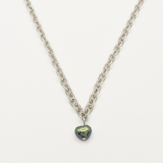 The Salty Dreamers "A Beach Pearl" necklace features a silver chain with a dark iridescent heart pendant and freshwater pearl accents, shown on a white background for surfer-inspired style.