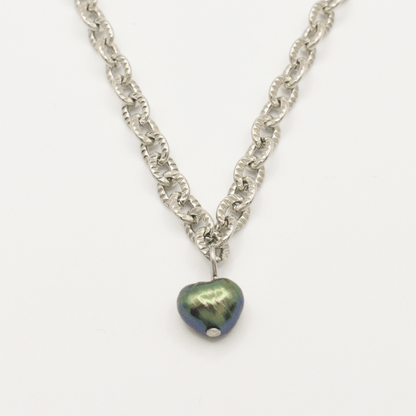 The "A Beach Pearl" necklace by Salty Dreamers features a silver chain and a dark iridescent heart pendant with a subtle surfer vibe, showcased against a white background.