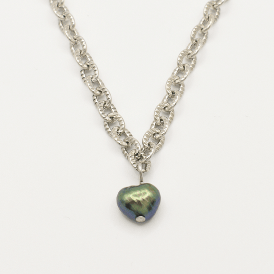 The "A Beach Pearl" necklace by Salty Dreamers features a silver chain and a dark iridescent heart pendant with a subtle surfer vibe, showcased against a white background.