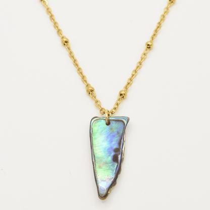 The Paua Shell Hine Necklace by Salty Dreamers features a gold chain with small beads and a triangular New Zealand abalone shell pendant, perfect for handmade jewelry enthusiasts.