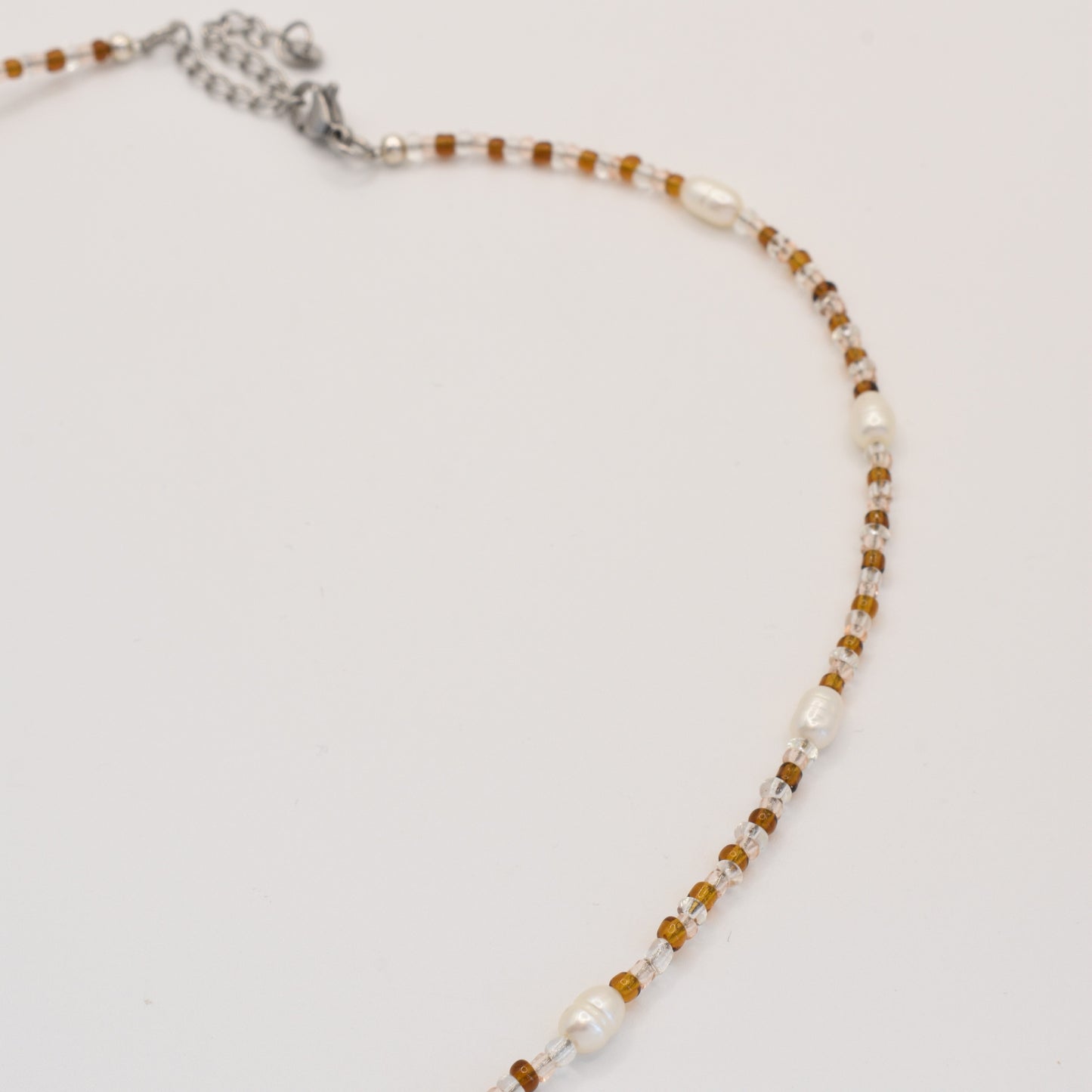 The Salty Dreamers Necklace | Caramel Whispers is a handmade piece featuring small brown beads, white freshwater pearls spaced along its length, and a silver clasp and chain, displayed on a white background.