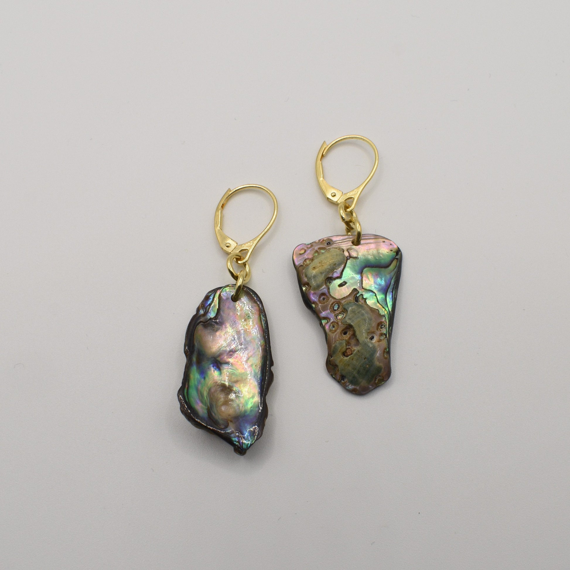The Salty Dreamers Earrings | Paua Shell Marie feature irregular, iridescent paua shell pendants with gold lever-back hooks, elegantly displayed on a plain white background—a stunning piece of New Zealand jewelry.