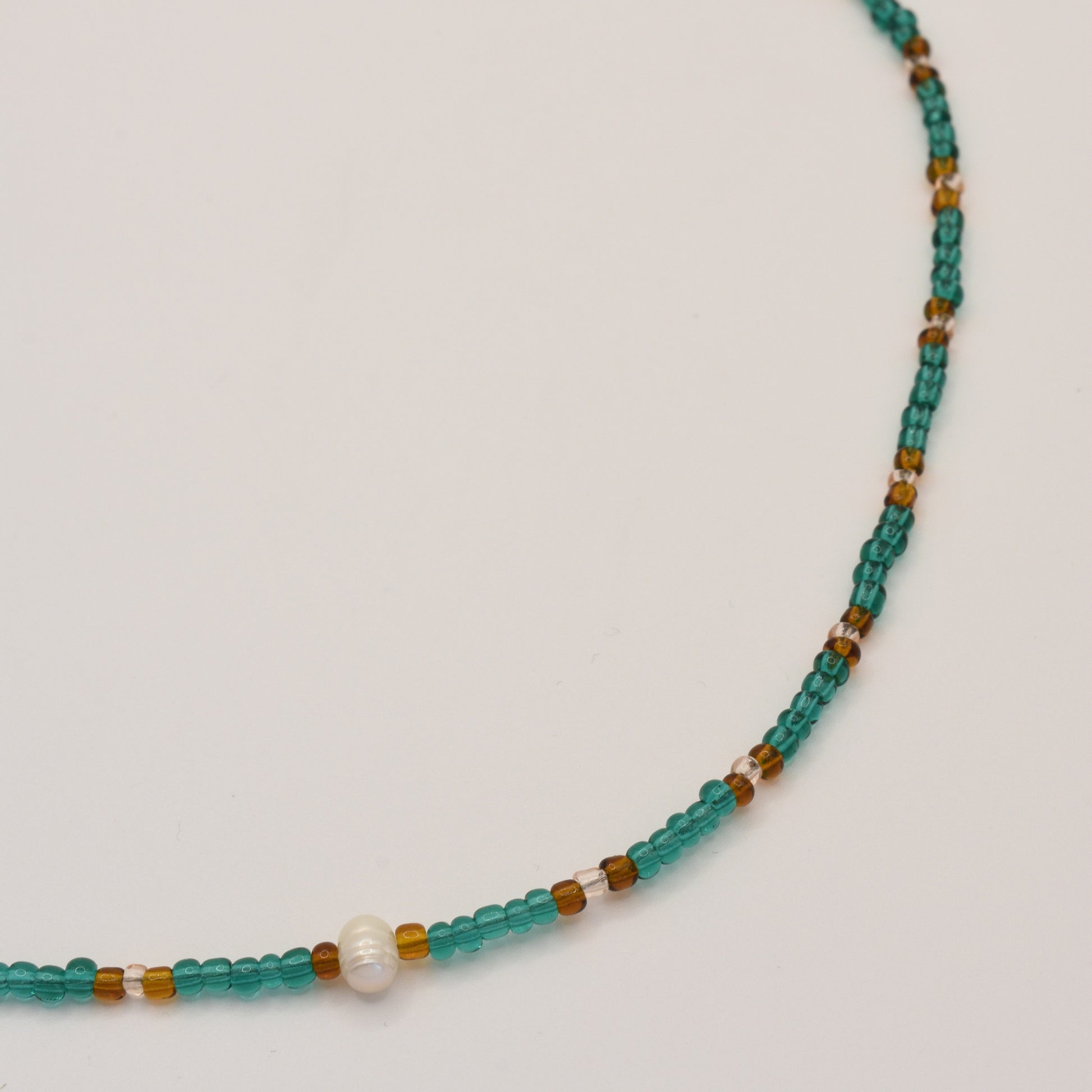 The Salty Dreamers Necklace | Fresh Beads Blue is a handmade jewellery piece featuring turquoise, amber-colored, and a single white bead, elegantly displayed on a plain white background.
