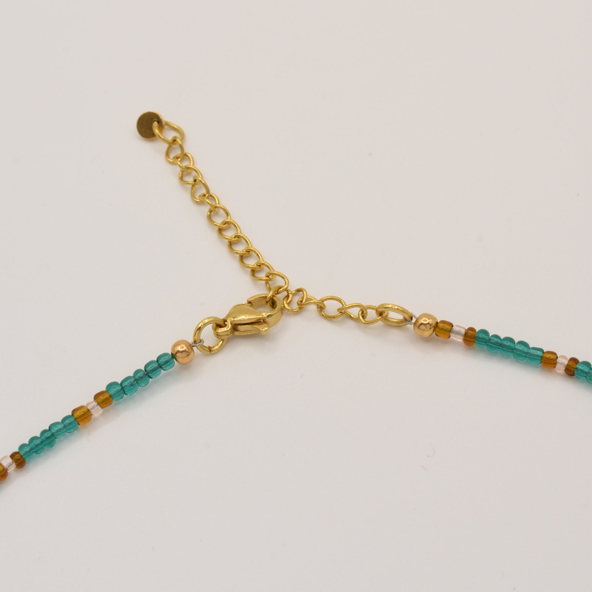 The Salty Dreamers Necklace | Fresh Beads Blue features small turquoise and amber beads with a gold lobster clasp and adjustable chain, displayed on a white background.