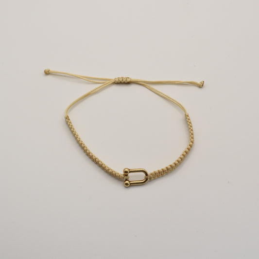 The Salty Dreamers Bracelet | Sailors Love Beige is a handmade beige macramé bracelet with a small gold-colored U-shaped charm, inspired by classic sailor shakel designs and shown on a plain white background.