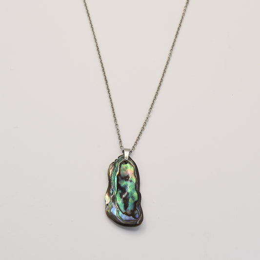 The Salty Dreamers Paua Shell Takaro Necklace features an irregularly shaped iridescent pāua shell pendant on a silver chain—a striking piece of New Zealand jewelry set against a plain white background.
