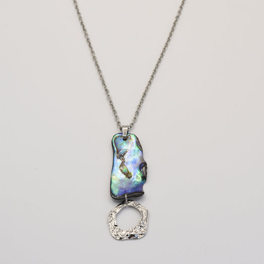 The Necklace | Paua Shell Atea by Salty Dreamers showcases a handmade silver chain with an iridescent, irregular paua shell pendant and a textured silver ring, displayed on a plain light background.