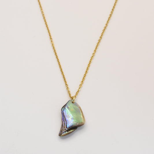 The Salty Dreamers Paua Shell Aroha Necklace features a gold chain with an irregular, iridescent pāua shell pendant, elegantly showcased on a white background.