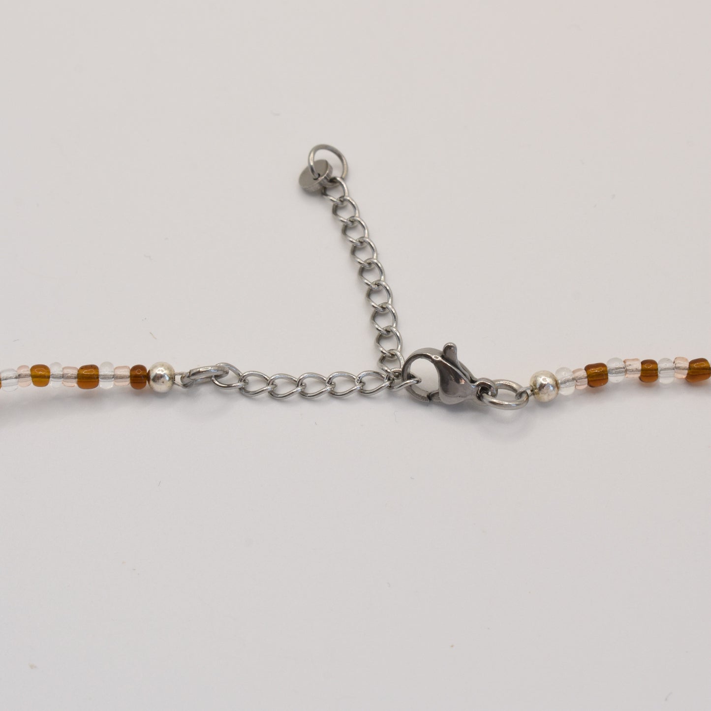 A close-up of the Salty Dreamers Necklace | Caramel Whispers shows its handmade clasp, metal chain extender, and small brown and clear beads against a white background.