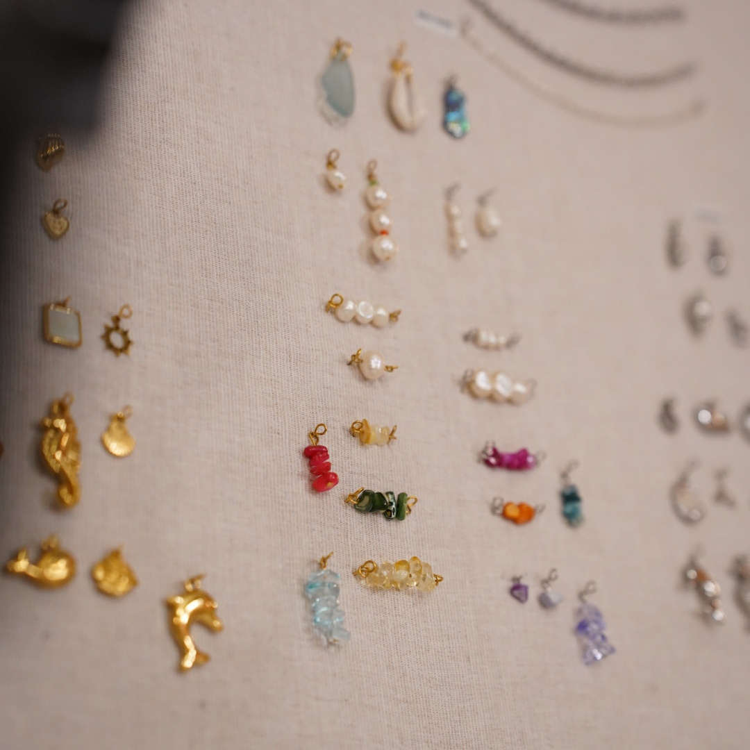 A selection of gold, colorful beaded, and pearl charms arranged on beige fabric—ideal inspiration for your own creations or for attending the Salty Dreamers' Workshop Ocean Jewellery in Kiel.