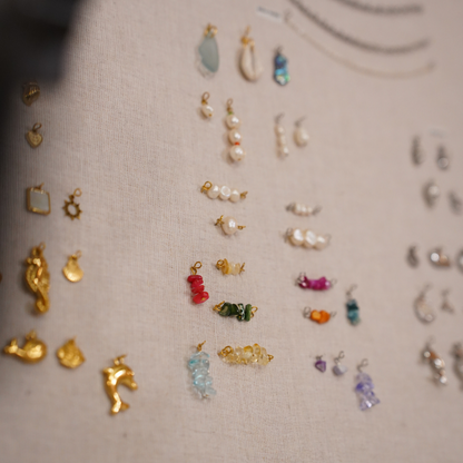 A selection of gold, colorful beaded, and pearl charms arranged on beige fabric—ideal inspiration for your own creations or for attending the Salty Dreamers' Workshop Ocean Jewellery in Kiel.